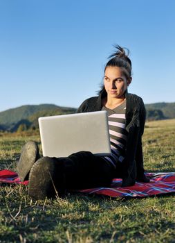 young teen woman work on laptop computer outdoor in nature with blue sky and green grass in background