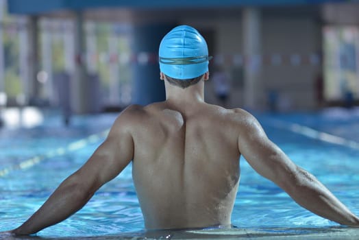 Happy muscular swimmer wearing glasses and cap at swimming pool and represent health and fit concept