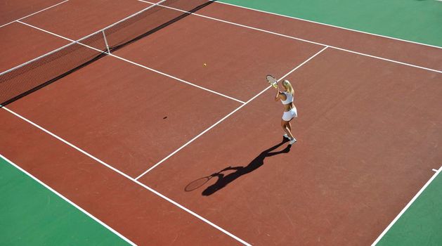 young fit woman play tennis outdoor on orange tennis field at early morning