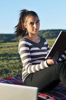 young teen girl read book and study homework outdoor in nature with blue sky in background