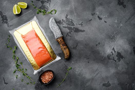 Salmon fillets in a vacuum package set, with herbs, on gray stone table background, top view flat lay, with copy space for text