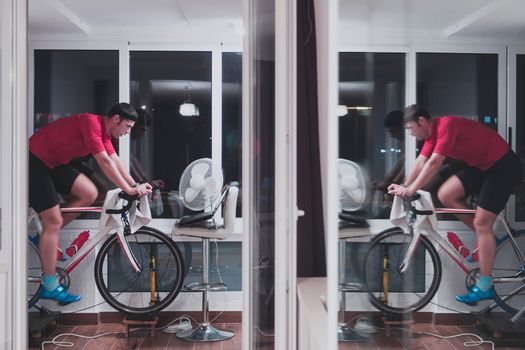 Man cycling on the machine trainer he is exercising in the home at night. Playing online bike racing game during coronavirus covid19 lockdown. New normal concept.