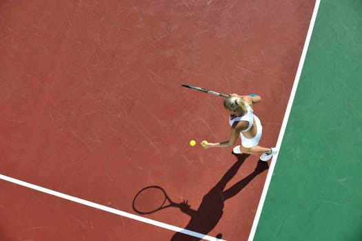 young fit woman play tennis outdoor on orange tennis field at early morning