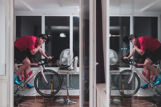 Man cycling on the machine trainer he is exercising in the home at night. Playing online bike racing game during coronavirus covid19 lockdown. New normal concept.