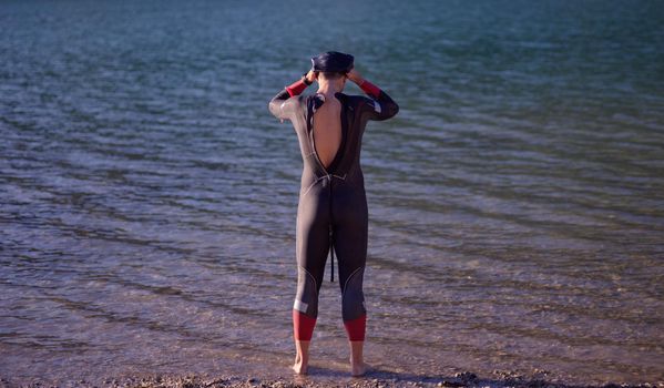 reak triathlon athlete getting ready and prepare goggles hat and  wetsuit for swimming training on lake