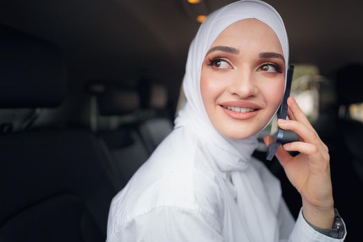 Beautiful young woman in hijab sitting in a car and talking on the phone, close up