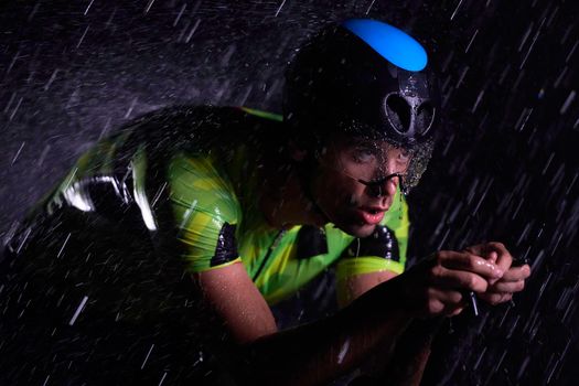 triathlon athlete riding professional racing bike fast  at night with bad weather and falling rain