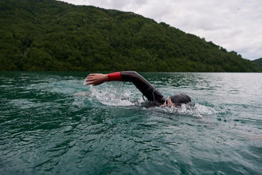 triathlon athlete swimming on extreme morning training in green lake wearing wetsuit