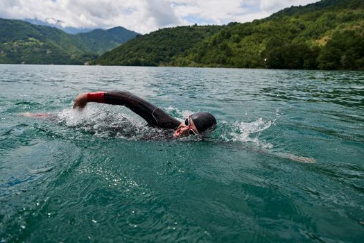 triathlon athlete swimming on extreme morning training in green lake wearing wetsuit