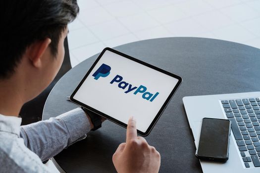 CHIANG MAI, THAILAND - NOV 28, 2021: Man holding a iPad with service PayPal on the screen.
