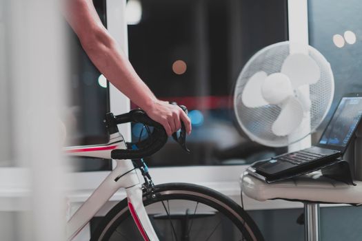 Man cycling on the machine trainer he is exercising in the home at night. Playing online bike racing game during coronavirus covid19 lockdown. New normal concept.