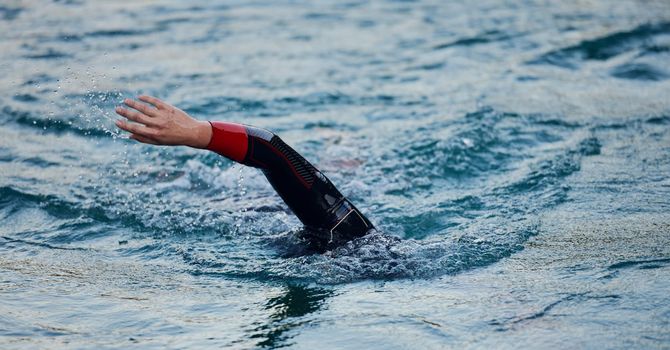 triathlon athlete swimming on beautiful morning sunrise training in lake wearing wetsuit concept of strength and endurance