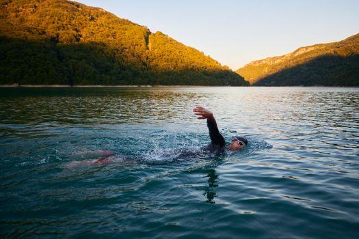 triathlon athlete swimming on beautiful morning sunrise training in lake wearing wetsuit concept of strength and endurance