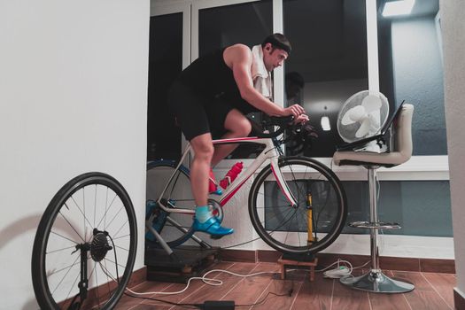 Man cycling on the machine trainer he is exercising in the home at night. Playing online bike racing game during coronavirus covid19 lockdown. New normal concept.