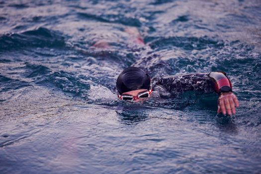 triathlon athlete swimming on beautiful morning sunrise training in lake wearing wetsuit concept of strength and endurance