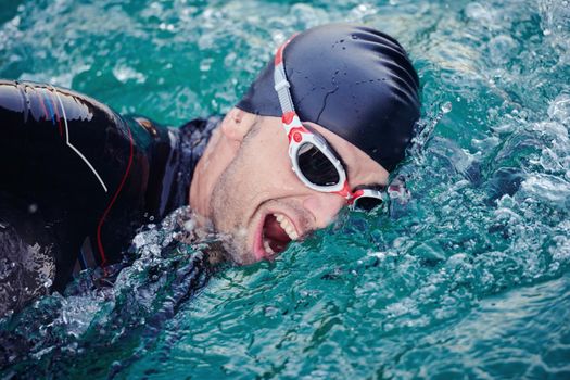 triathlon athlete swimming on beautiful morning sunrise training in lake wearing wetsuit concept of strength and endurance