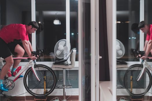 Man cycling on the machine trainer he is exercising in the home at night. Playing online bike racing game during coronavirus covid19 lockdown. New normal concept.