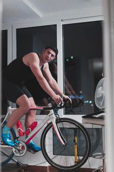 Man cycling on the machine trainer he is exercising in the home at night. Playing online bike racing game during coronavirus covid19 lockdown. New normal concept.