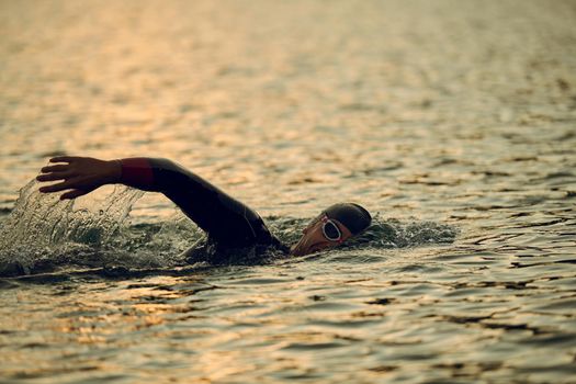 triathlon athlete swimming on beautiful morning sunrise training in lake wearing wetsuit concept of strength and endurance