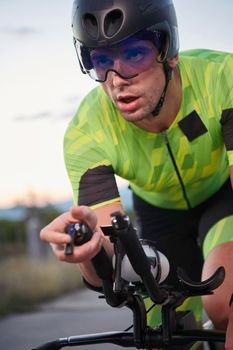 triathlon athlete riding professional racing bike on morning workout sunset or sunrise in background