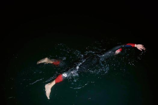 triathlon swimmer have extreme training  on dark night wearing wetsuit concept of strength and endurance