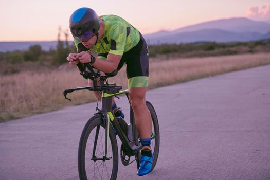 triathlon athlete riding professional racing bike on morning workout sunset or sunrise in background