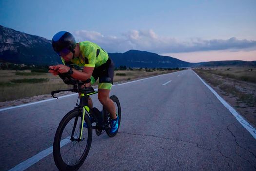 triathlon athlete riding professional racing bike at night workout on curvy country road w