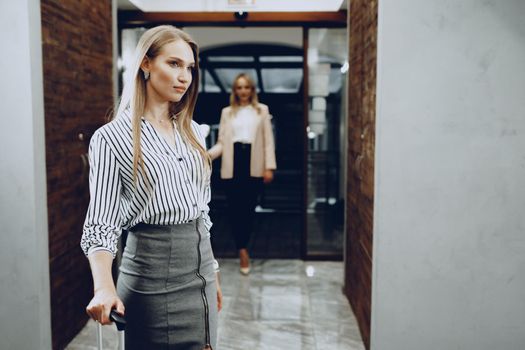 Two young women in formal clothes entering hotel lobby. Business trip concept