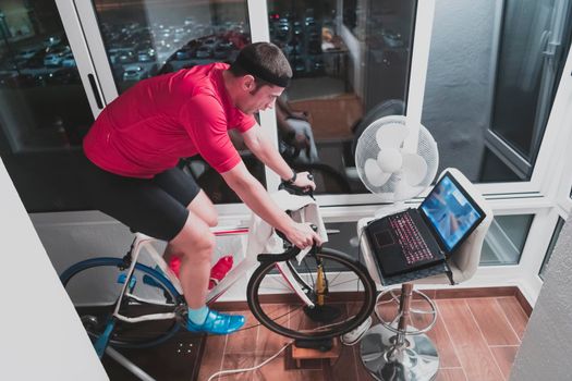 Man cycling on the machine trainer he is exercising in the home at night. Playing online bike racing game during coronavirus covid19 lockdown. New normal concept.