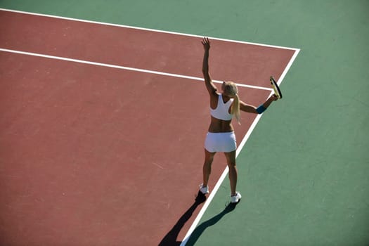 young fit woman play tennis outdoor on orange tennis field at early morning