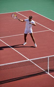 young man play tennis outdoor on orange tennis field at early morning