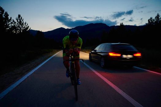 triathlon athlete riding professional racing bike at night workout on curvy country road w