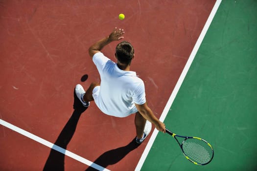 young man play tennis outdoor on orange tennis court at early morning