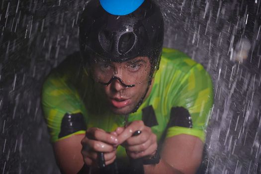 triathlon athlete riding professional racing bike fast  at night with bad weather and falling rain