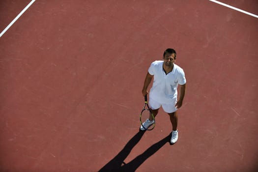 young man play tennis outdoor on orange tennis field at early morning