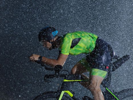 triathlon athlete riding professional racing bike at night with bad weather and falling rain