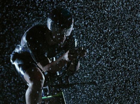 triathlon athlete riding professional racing bike at night with bad weather and falling rain