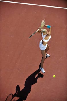 young fit woman play tennis outdoor on orange tennis field at early morning