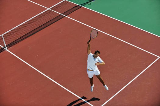 young man play tennis outdoor on orange tennis field at early morning