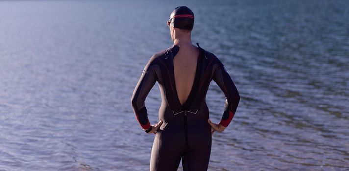 reak triathlon athlete getting ready and prepare goggles hat and  wetsuit for swimming training on lake