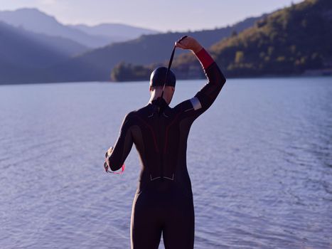 reak triathlon athlete getting ready and prepare goggles hat and  wetsuit for swimming training on lake