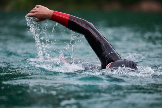 triathlon athlete swimming on extreme morning training in green lake wearing wetsuit