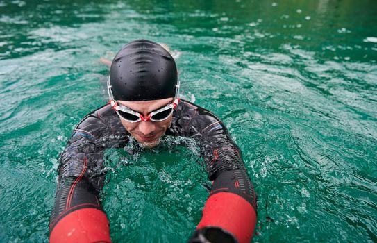 triathlon athlete swimming on extreme morning training in green lake wearing wetsuit