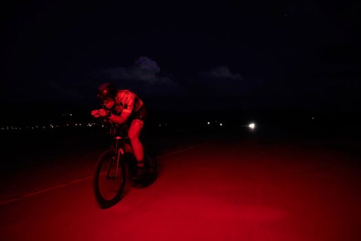 triathlon athlete cycling fast riding professional racing bike at night neon color gel lights