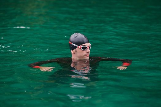 triathlon athlete swimming on extreme morning training in green lake wearing wetsuit