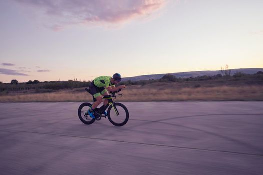 triathlon athlete riding professional racing bike on morning workout sunset or sunrise in background