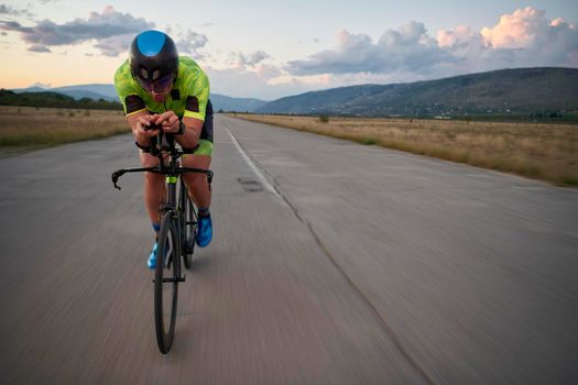 triathlon athlete riding professional racing bike on morning workout sunset or sunrise in background