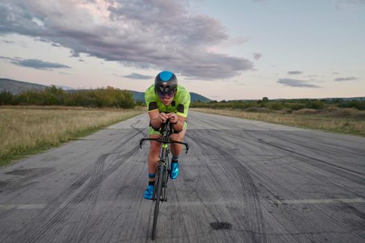 triathlon athlete riding professional racing bike on morning workout sunset or sunrise in background