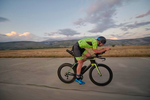 triathlon athlete riding professional racing bike on morning workout sunset or sunrise in background