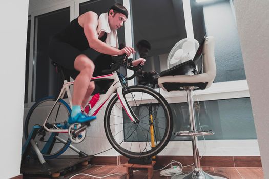 Man cycling on the machine trainer he is exercising in the home at night. Playing online bike racing game during coronavirus covid19 lockdown. New normal concept.